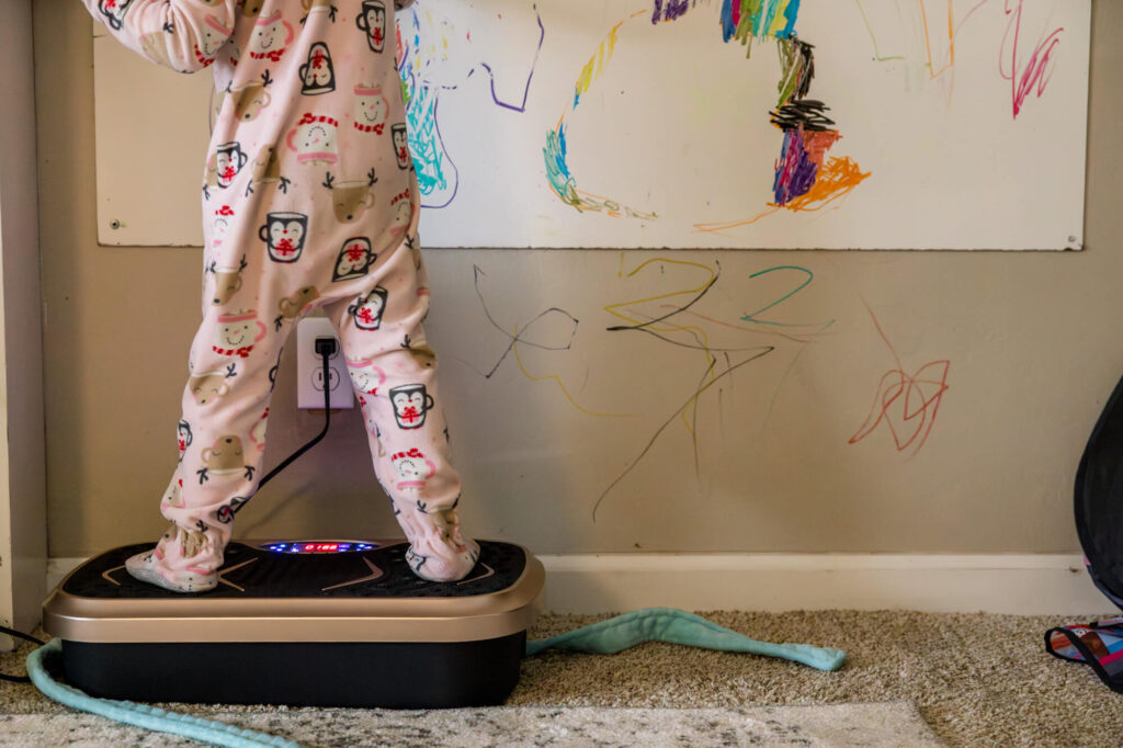 Little girl standing on exercise board while coloring on white board with marker lines on the wall