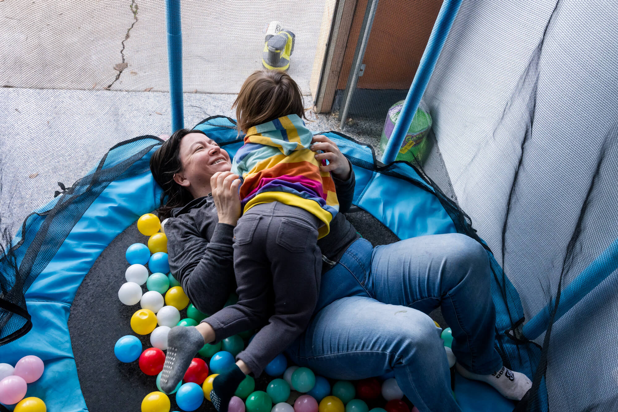 Mom laying on trampoline with plastic balls smiling at daughter who is laying on top