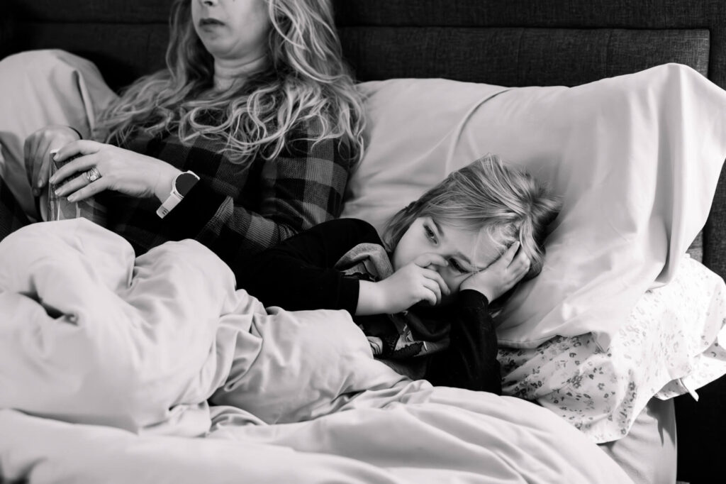Young girl in pajamas snuggled in bed with her mom, sucking her thumb during a documentary family photography session in Carmichael, CA.