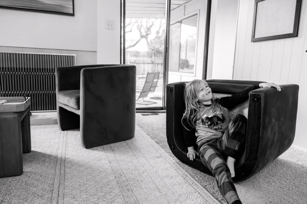 Little girl sitting in a knocked over chair in a silly way during a documentary session in Carmichael, CA