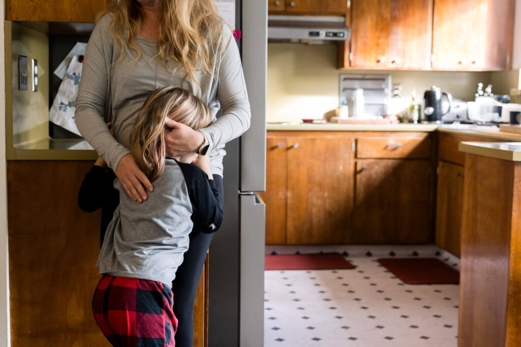 Mom hugging daughter in a quiet moment in their kitchen during a family documentary photography session.