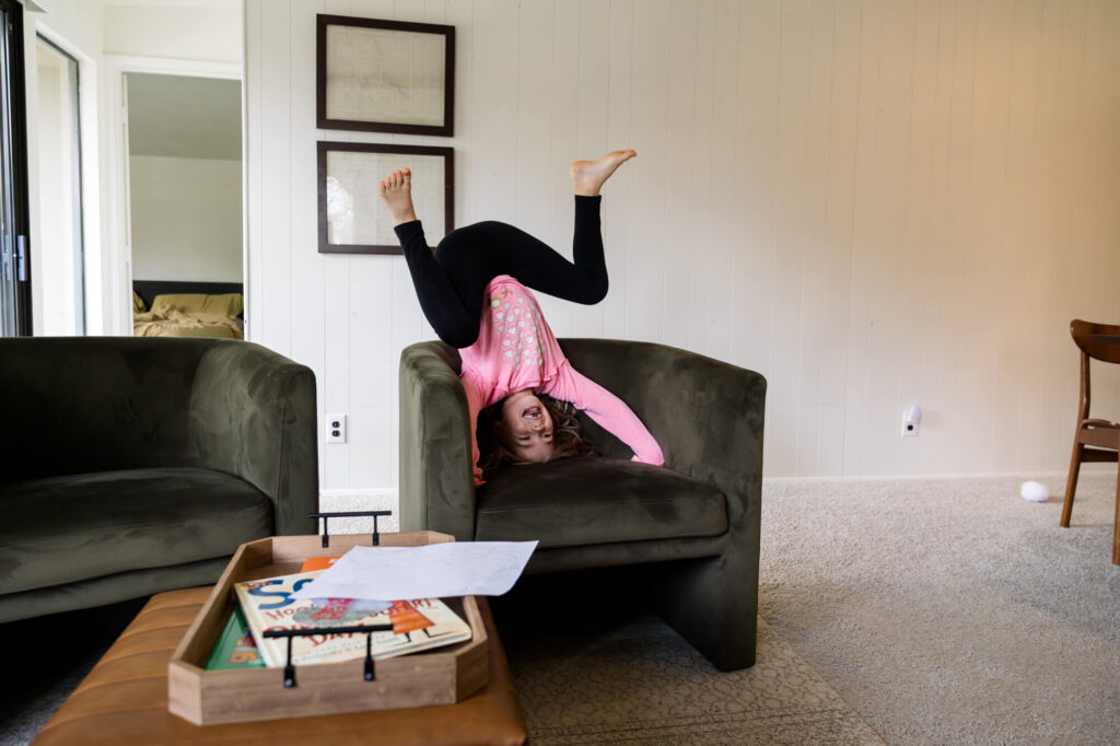 Little girl sitting upside down with legs in the air in an armchair, laughing