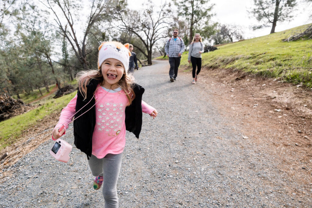 Little girl running toward the camera with family in the background walking down the nature trail to Hidden Falls, Auburn