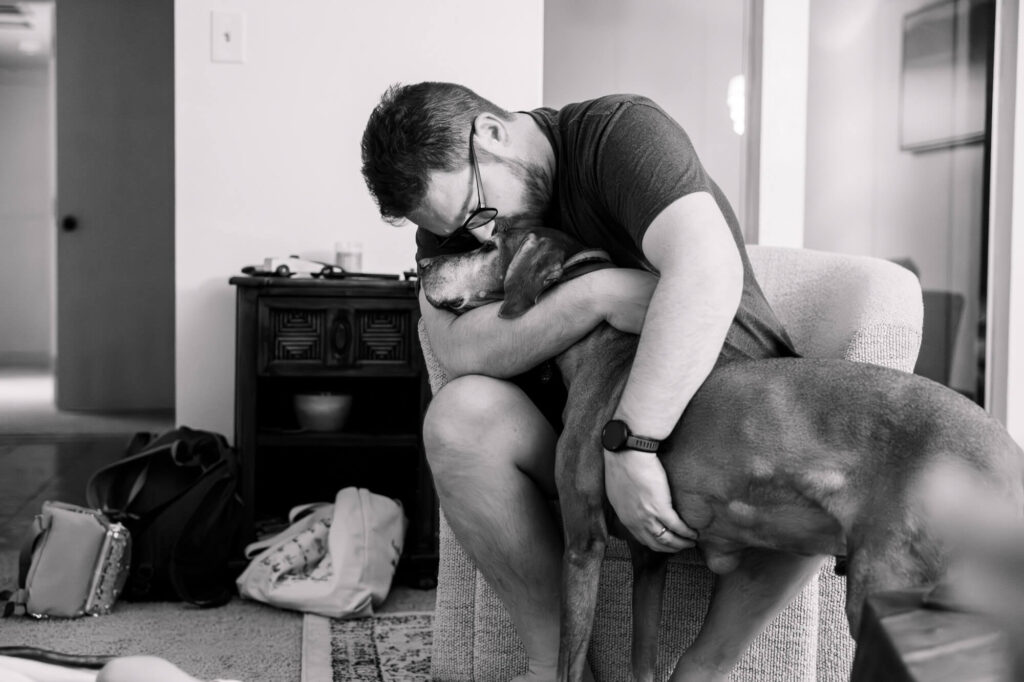 Man with arms wrapped around old dog, kissing him on the top of the head during a family documentary photography session